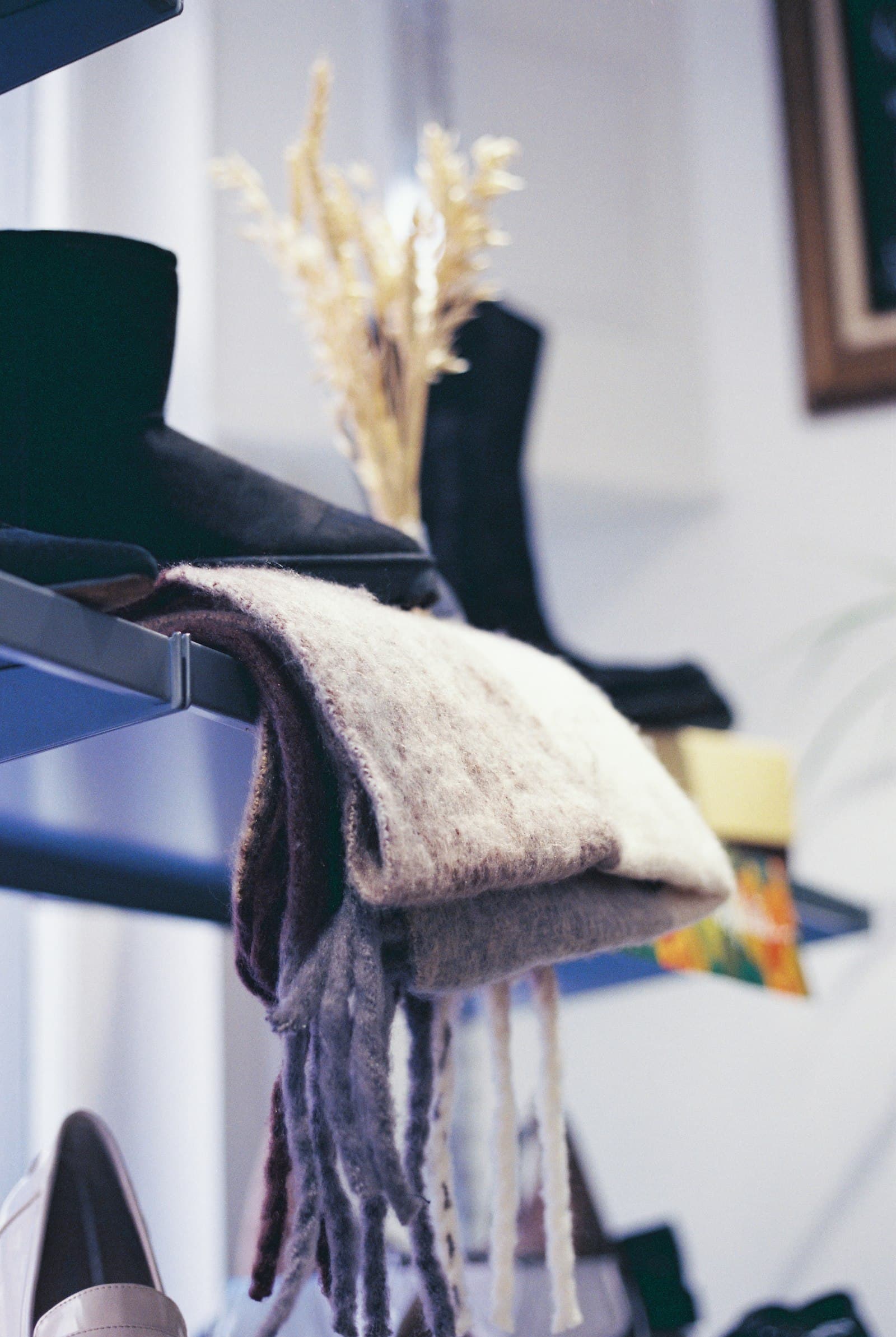 A knitted scarf draped over a shelf beside dried wheat stems and boots