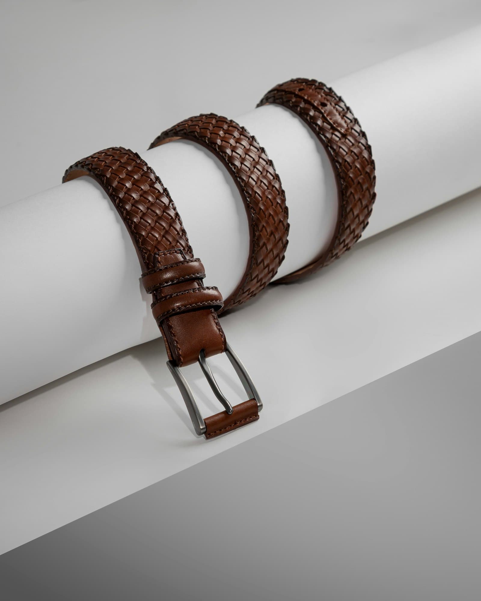A pair of brown leather belts sitting on top of a white piece of paper